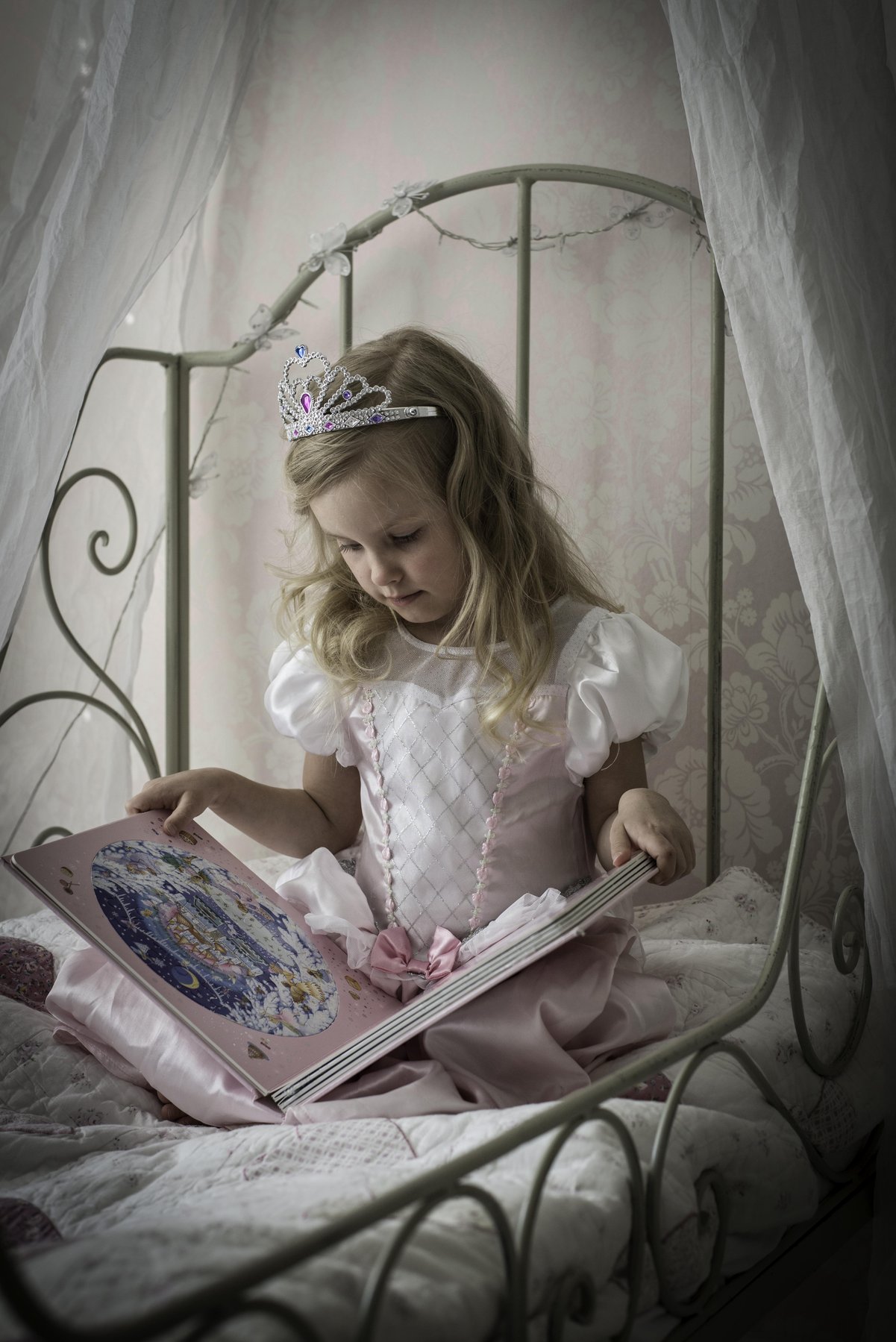 Tyttö prinsessamekossa lukemassa kuvakirjaa